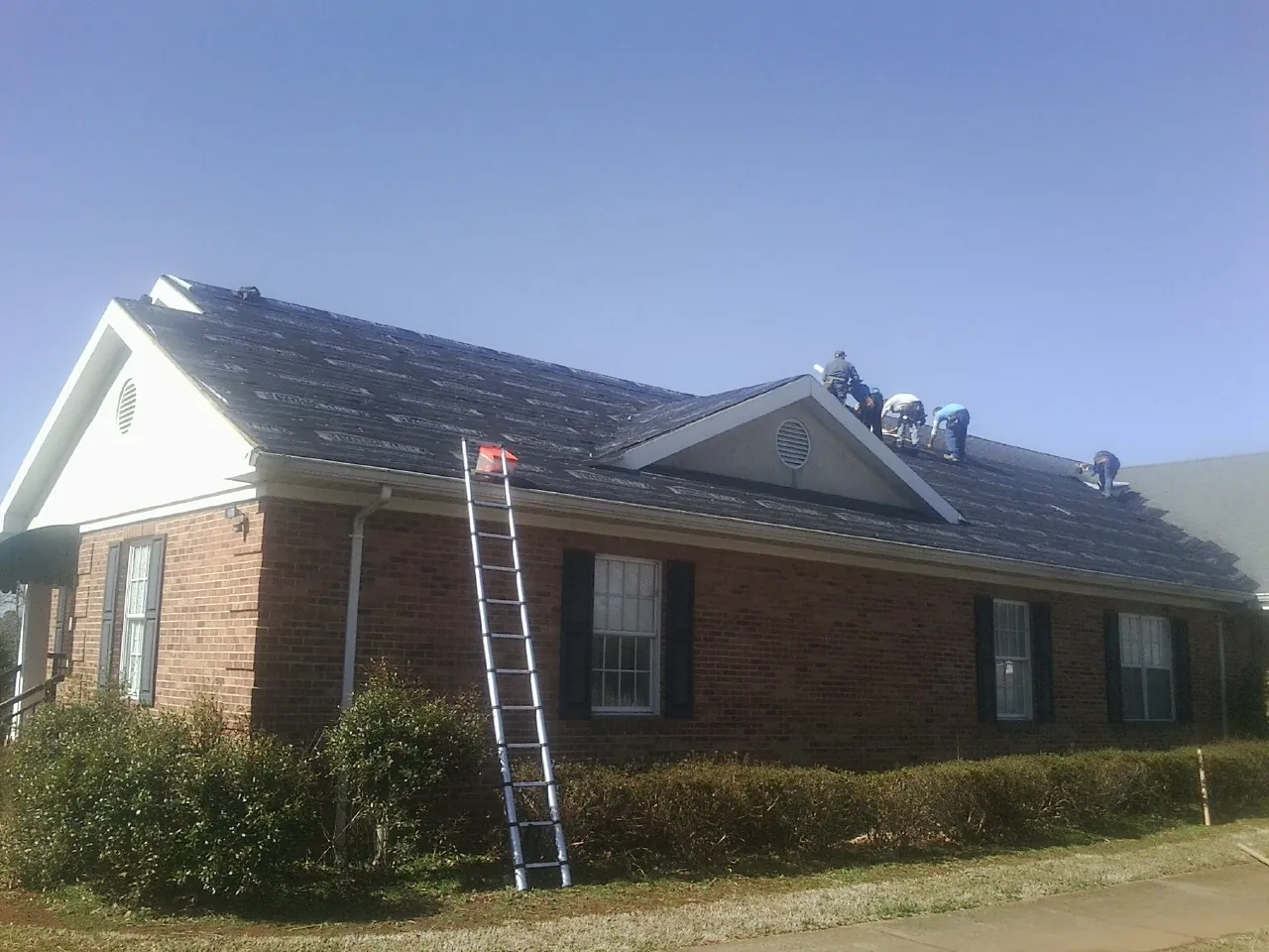 Crew tearing shingles off a brick ranch roof with a ladder set — Emergency Roof Repair work by our crew in Pierson