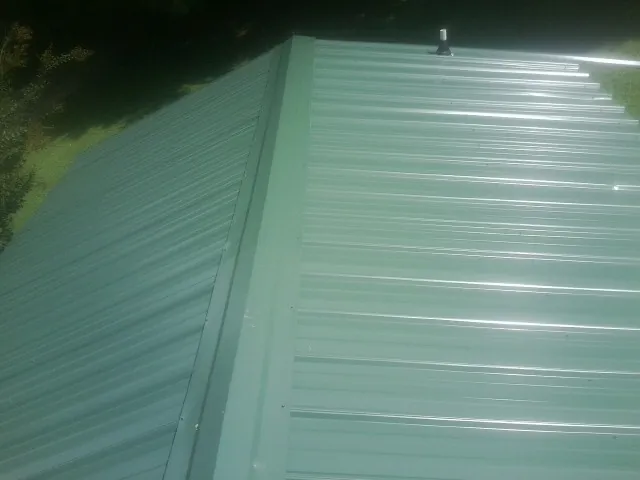 New green metal panels meeting at the ridge of a roof — Flat Roof Repair work by our crew in Pierson