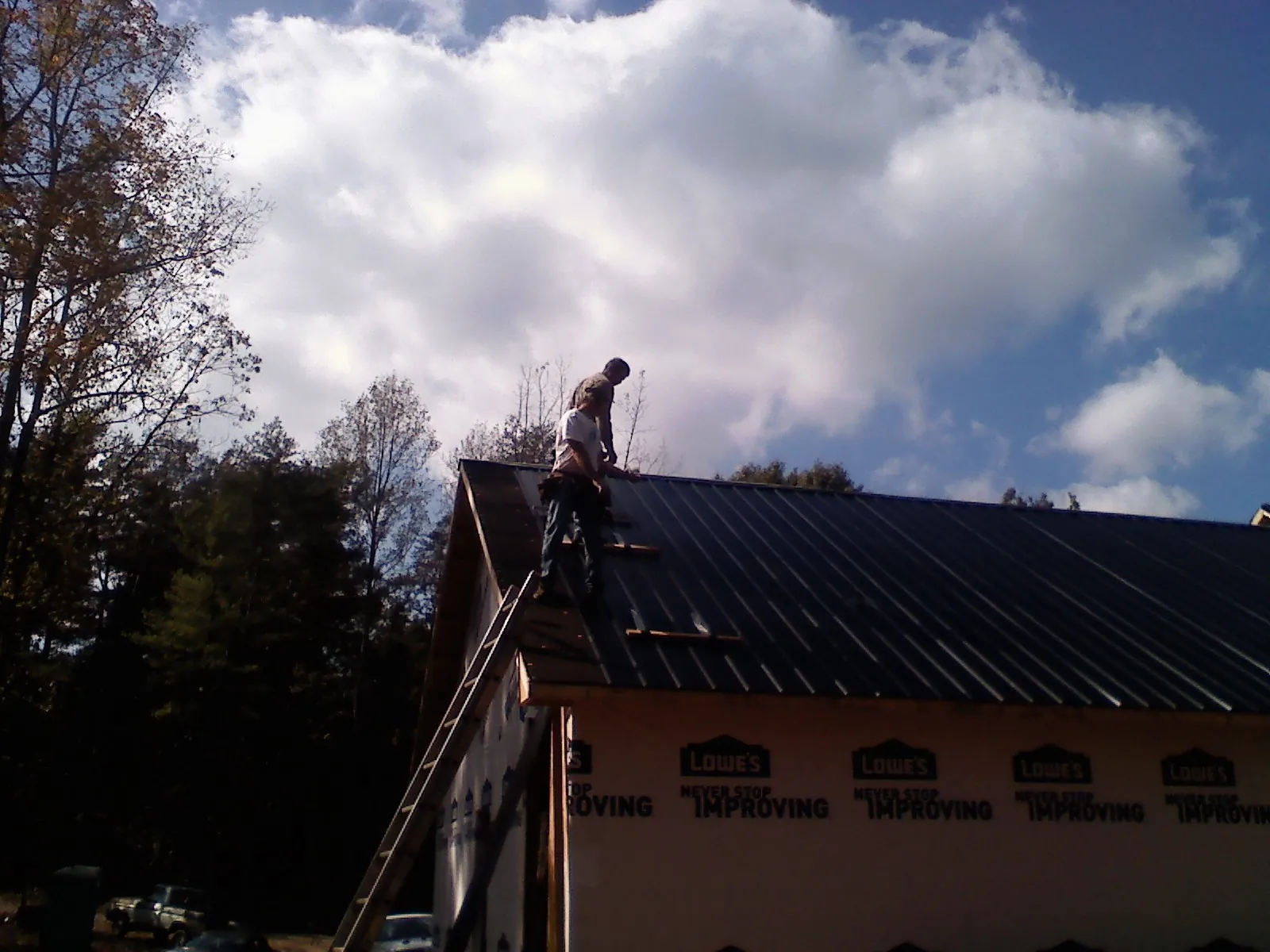 Roofer fastening dark metal panels high against a cloudy sky, from a Roof Inspection job in Pierson