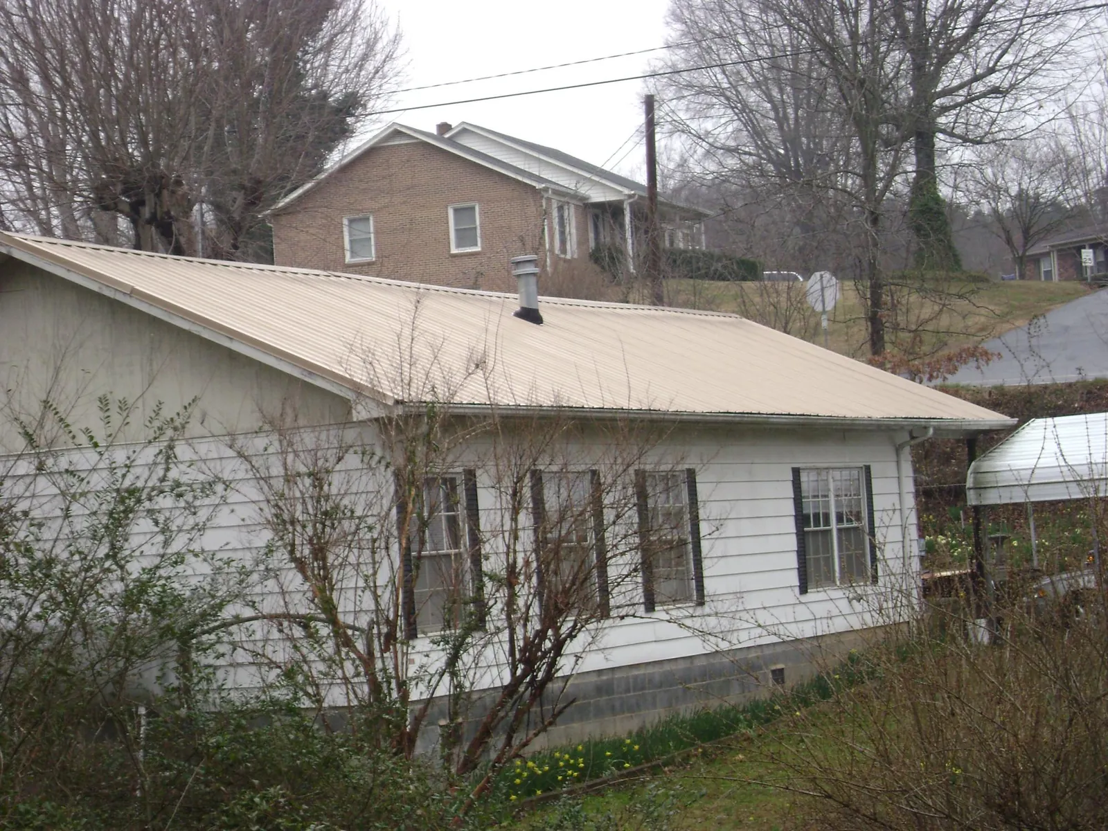 Tan metal roof on a white sided house set into a hillside — Commercial Roofing by Roofing Brothers in Pierson