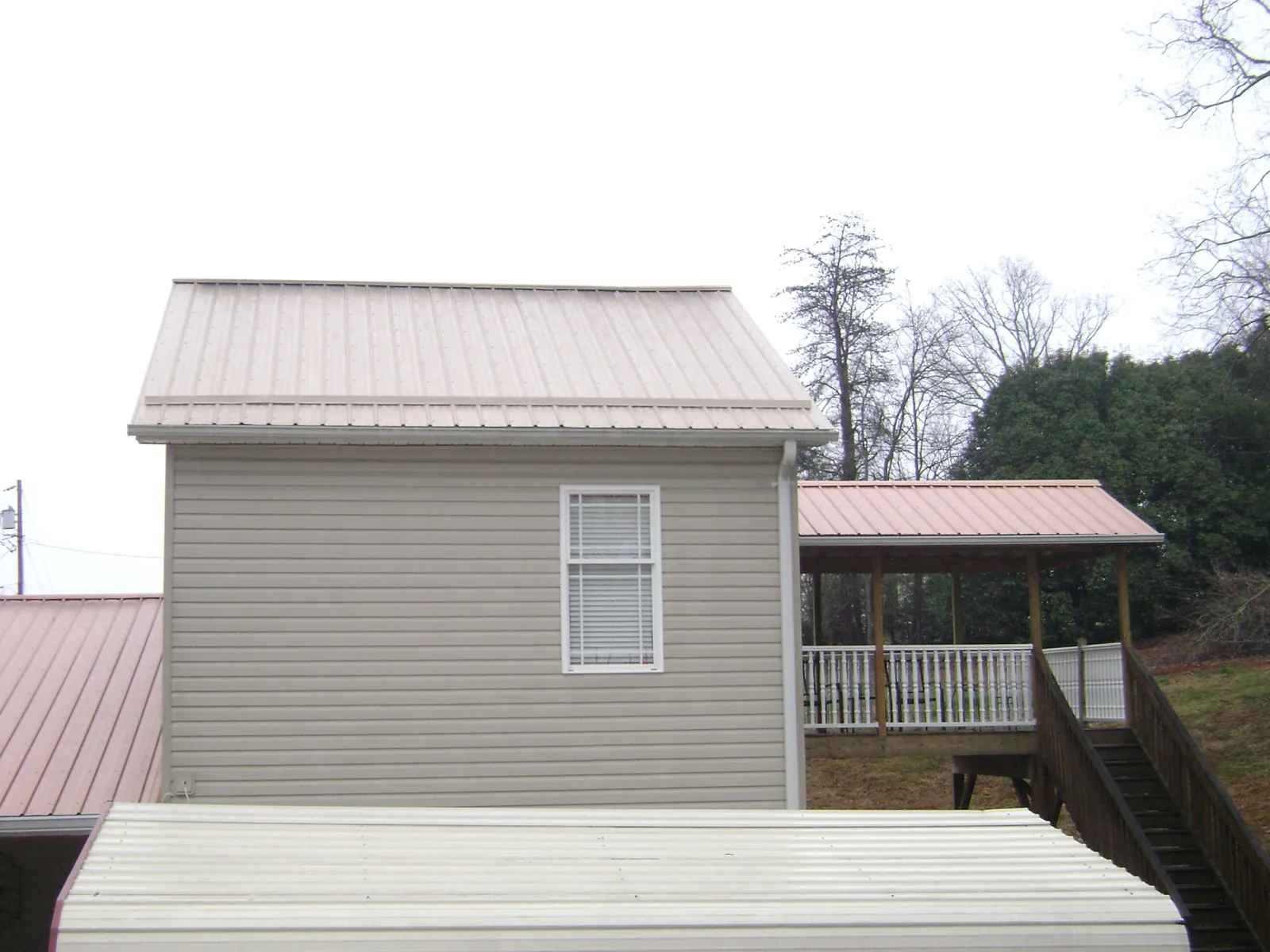 Tan metal roofs on a two story addition and attached porch, from a Roof Replacement job in Pierson